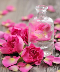 Photo d’un flacon d’eau de rose posé sur une table en bois couvert de roses et de pétales de roses Photo d’un flacon d’eau de rose posé sur une table en bois couvert de roses et de pétales de roses